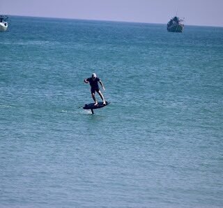 Man riding an electric surfboard above the water during a Bali watersport adventure, with boats visible in the background.
